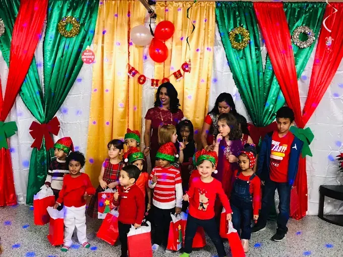 Group of children posing on a decorated stage with colorful curtains and balloons, many in red outfits