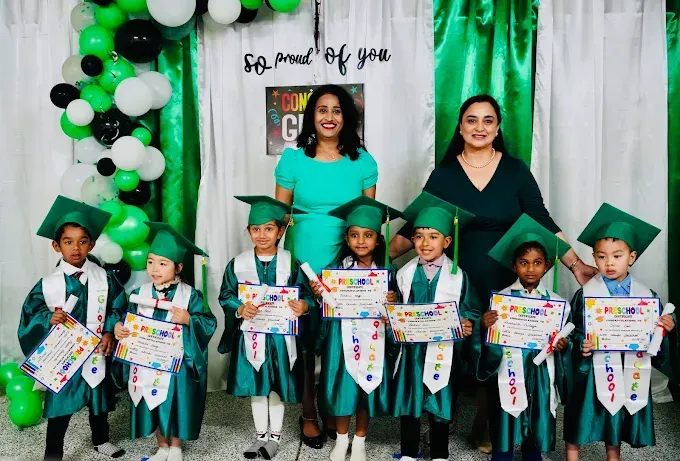 Graduation ceremony with teacher and children holding certificates in green caps and gowns