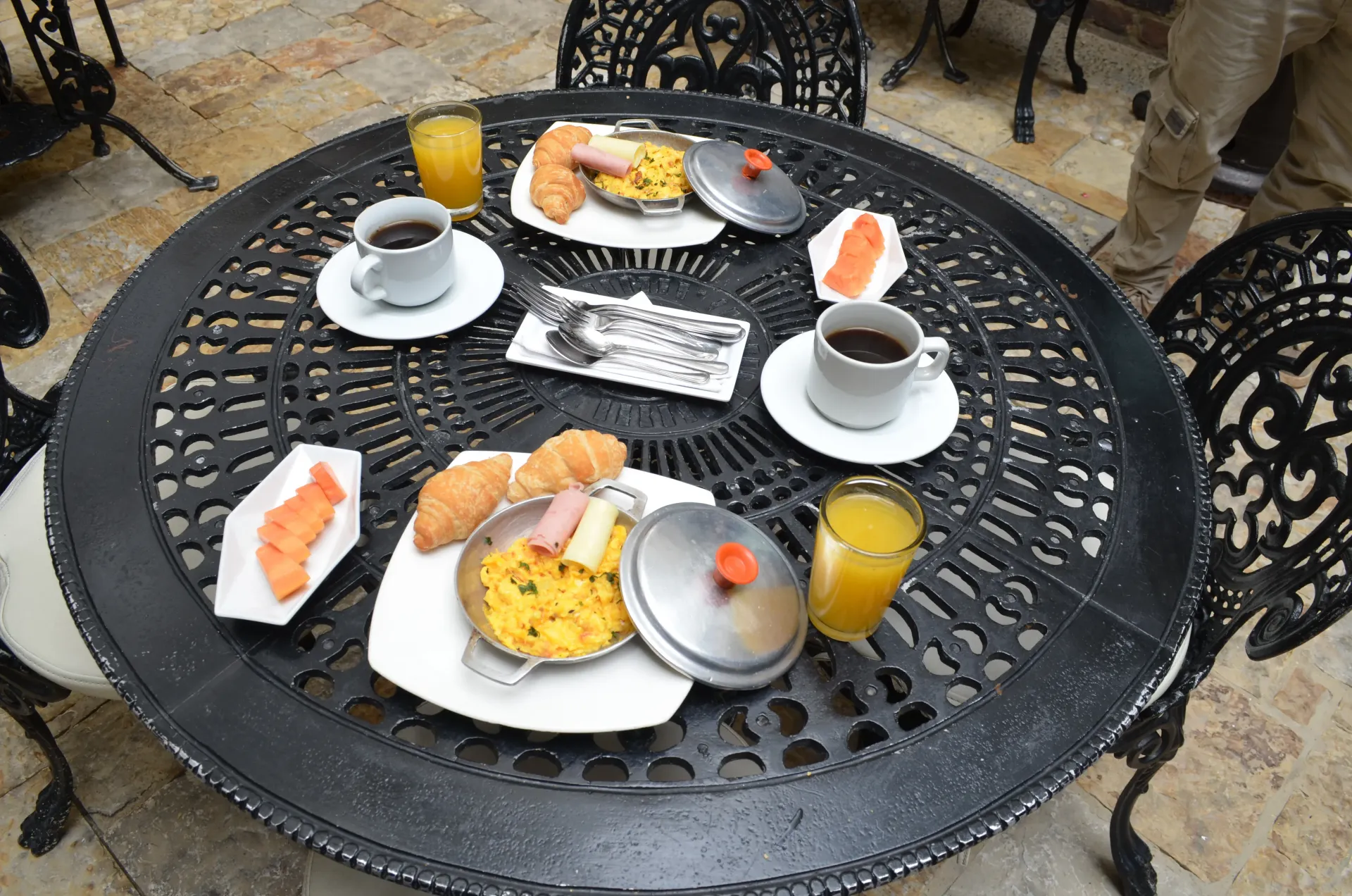 Mesa de desayuno con dos cubiertos: tortillas, cruasanes, zumo de naranja, café y salmón ahumado.