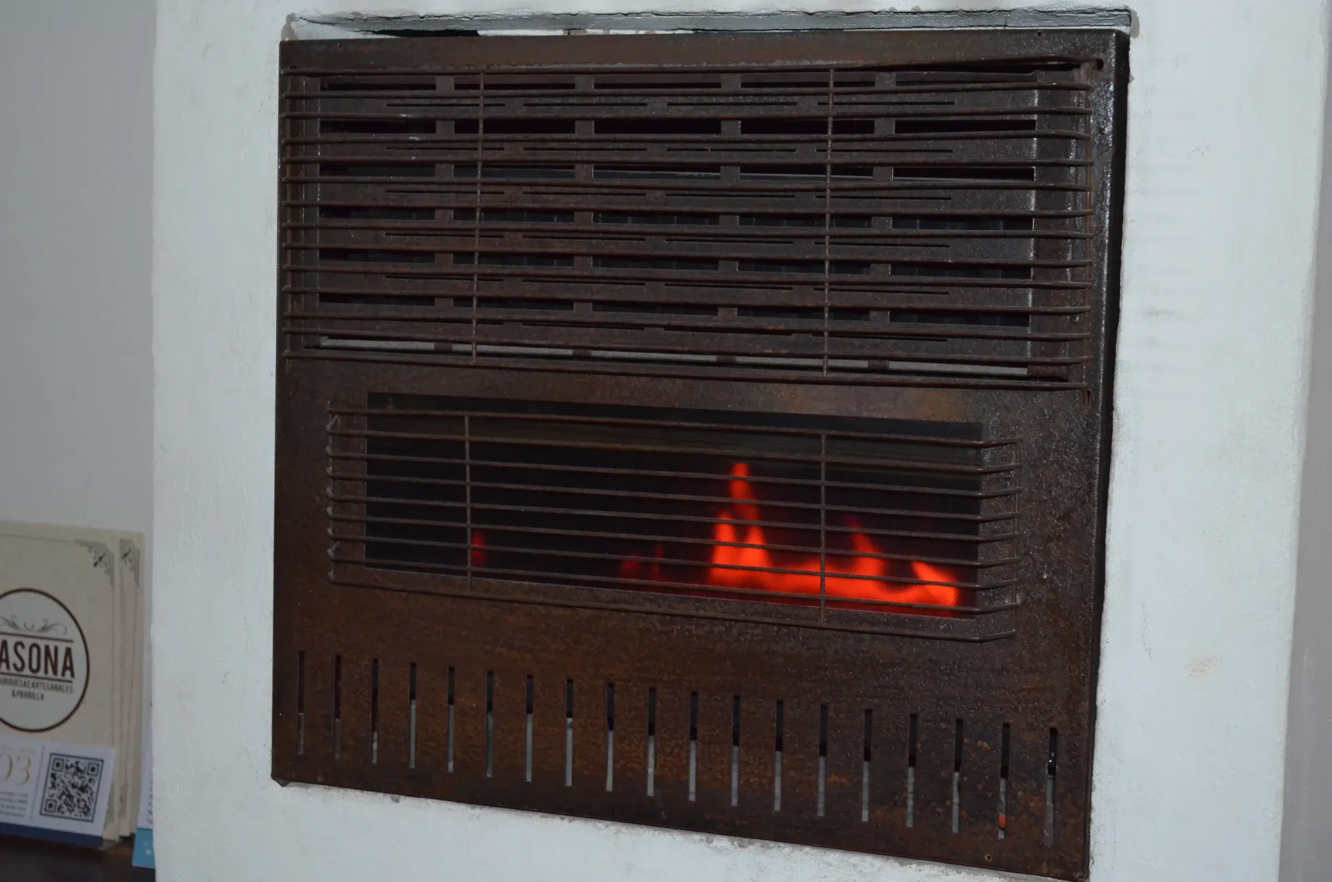 A wall-mounted heater with orange flames visible behind a dark metal grill.