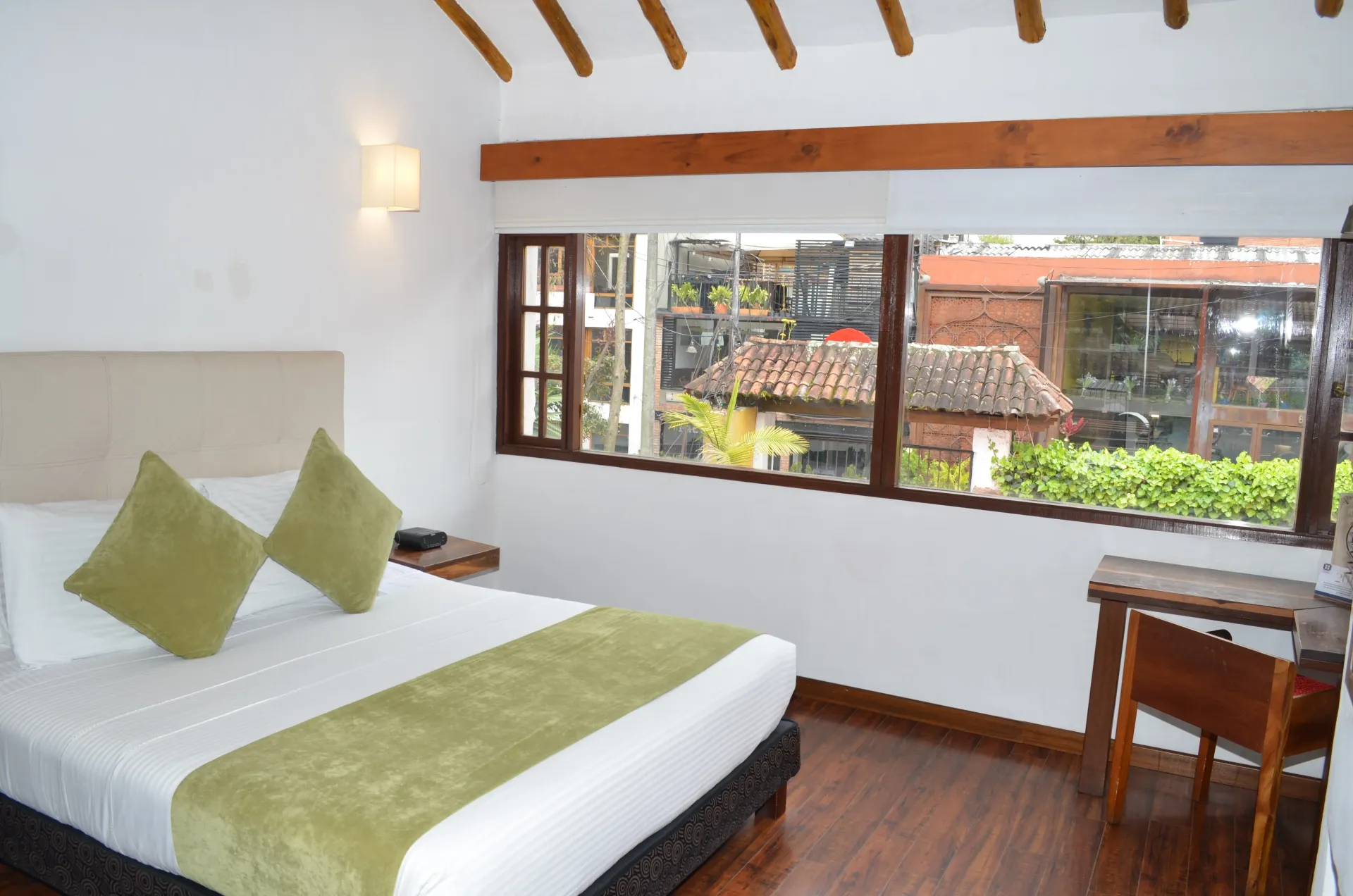 Hotel room with bed, window overlooking buildings, green accents.