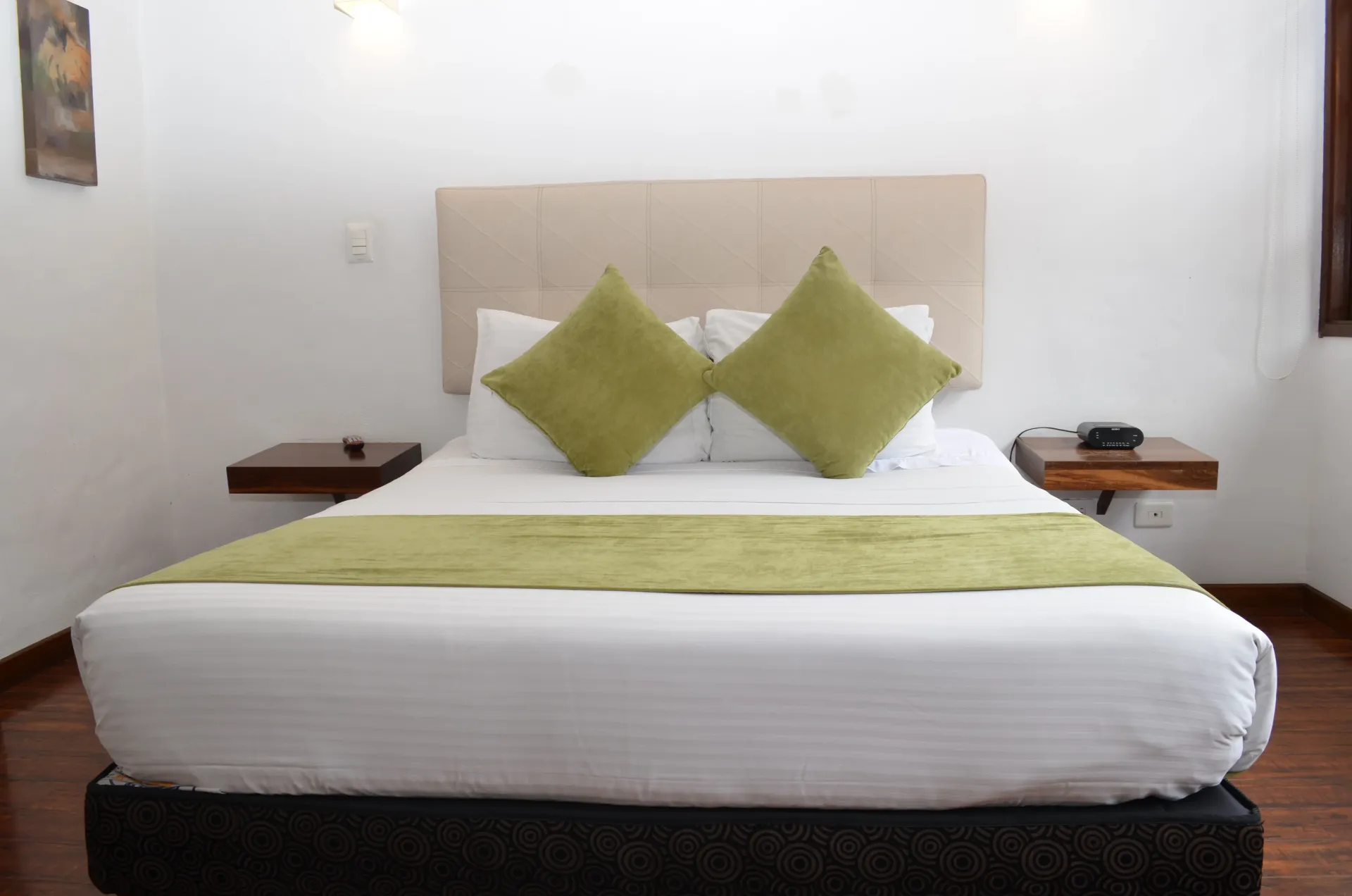Bedroom with white walls, king bed with green accents, and two floating nightstands.