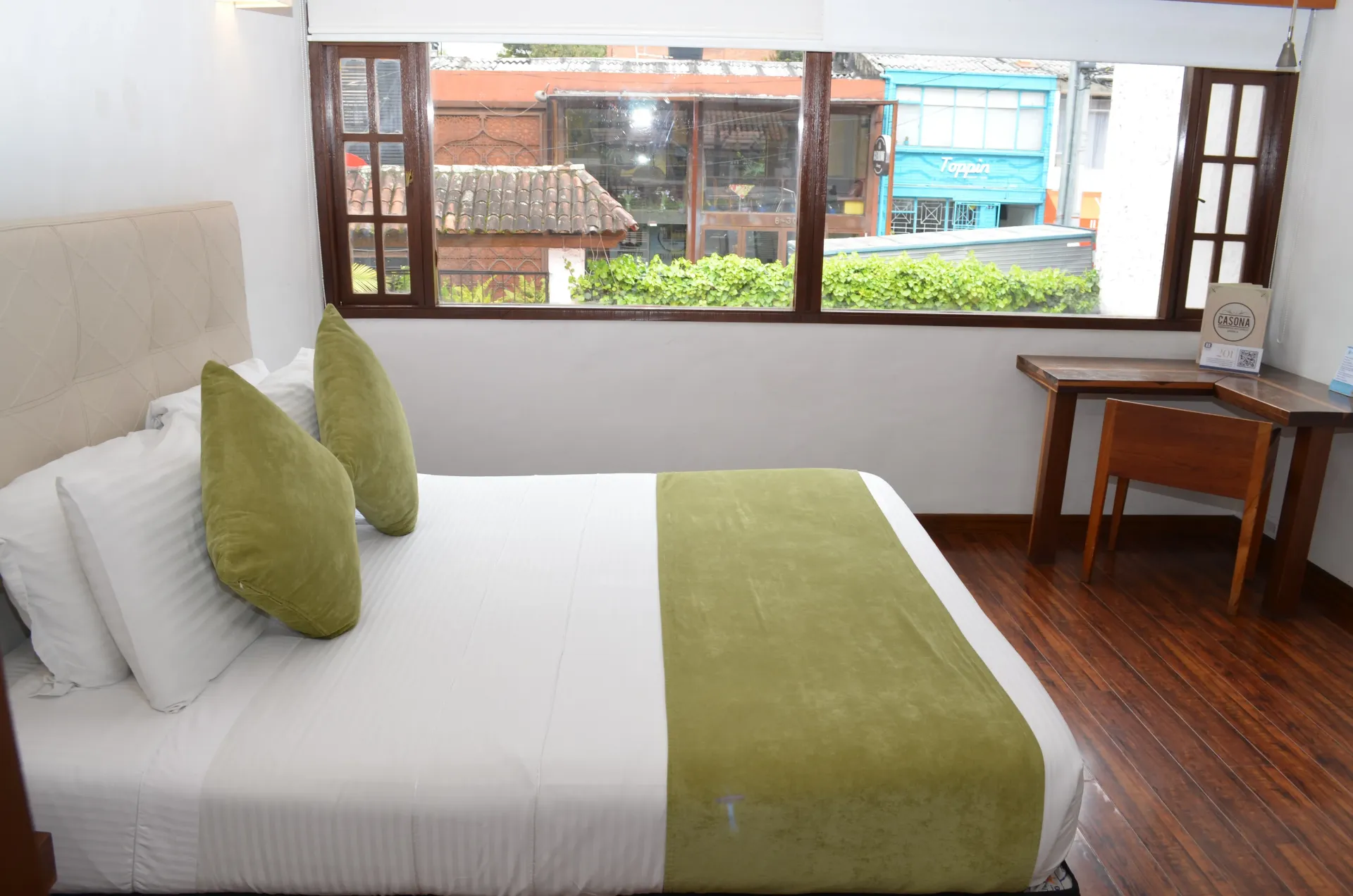 Bedroom with bed, desk, and window overlooking a street.