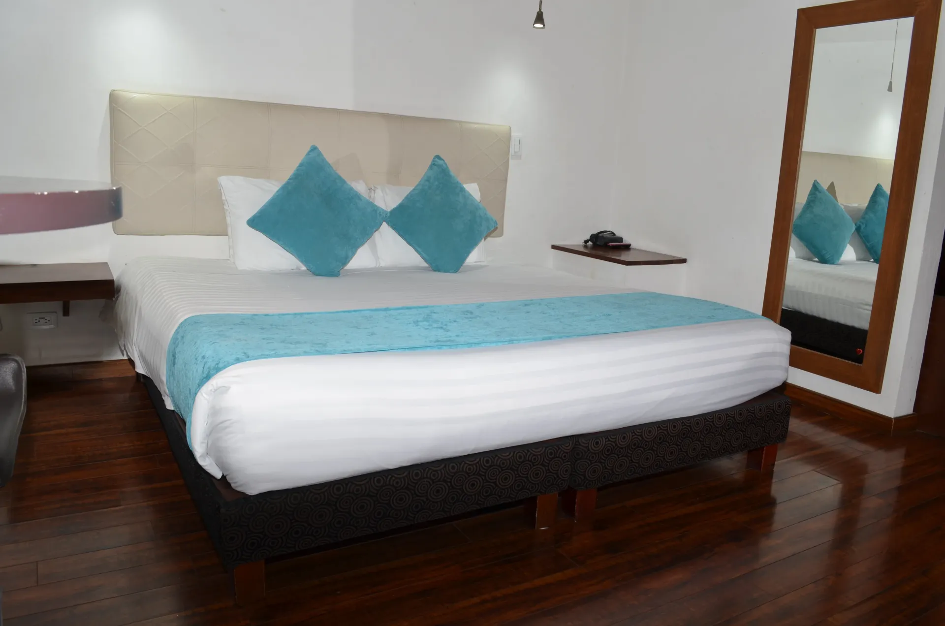 Hotel bedroom with a bed, pillows, and a large mirror. Turquoise accents on a white bedspread.