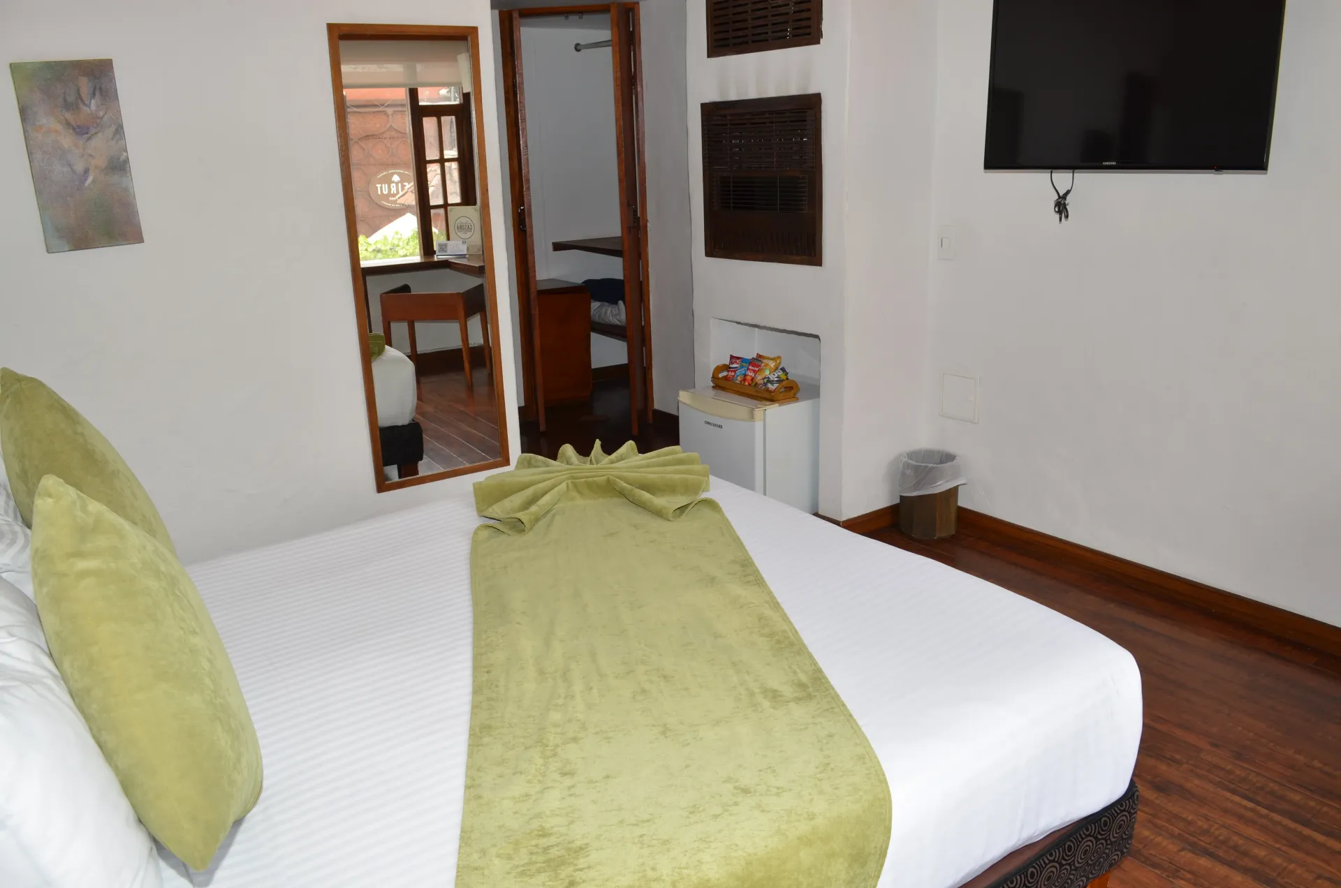 Bedroom with white bed, green pillows, and an open doorway to another room.