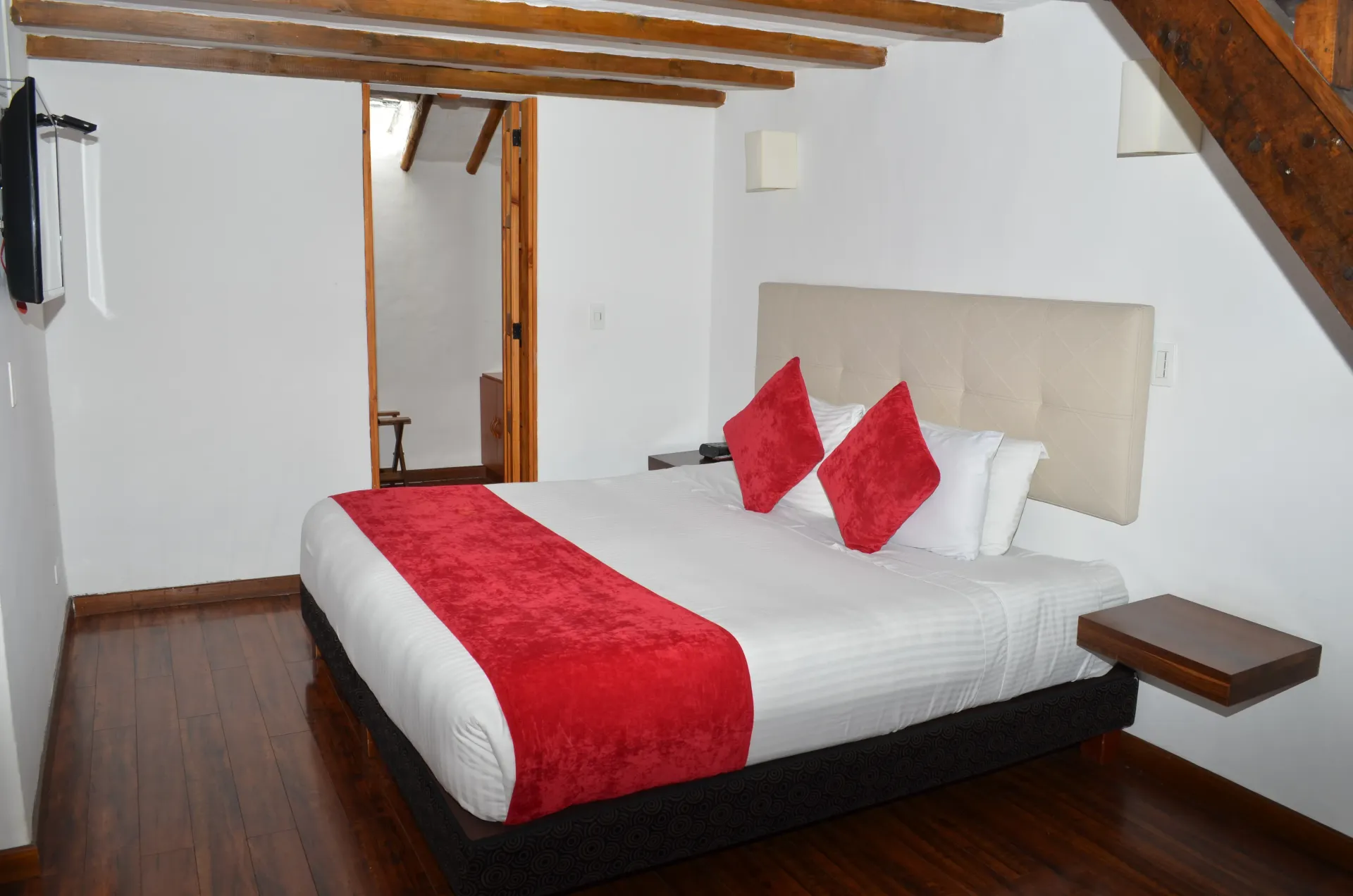Bedroom with a bed, red accents, and wooden beams. Open doorway to a bathroom is visible.
