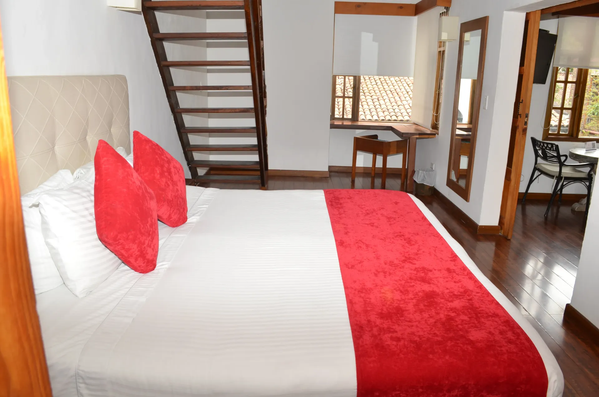 Dormitorio con cama, almohadas rojas y alfombra, escalera de madera y un pequeño escritorio.
