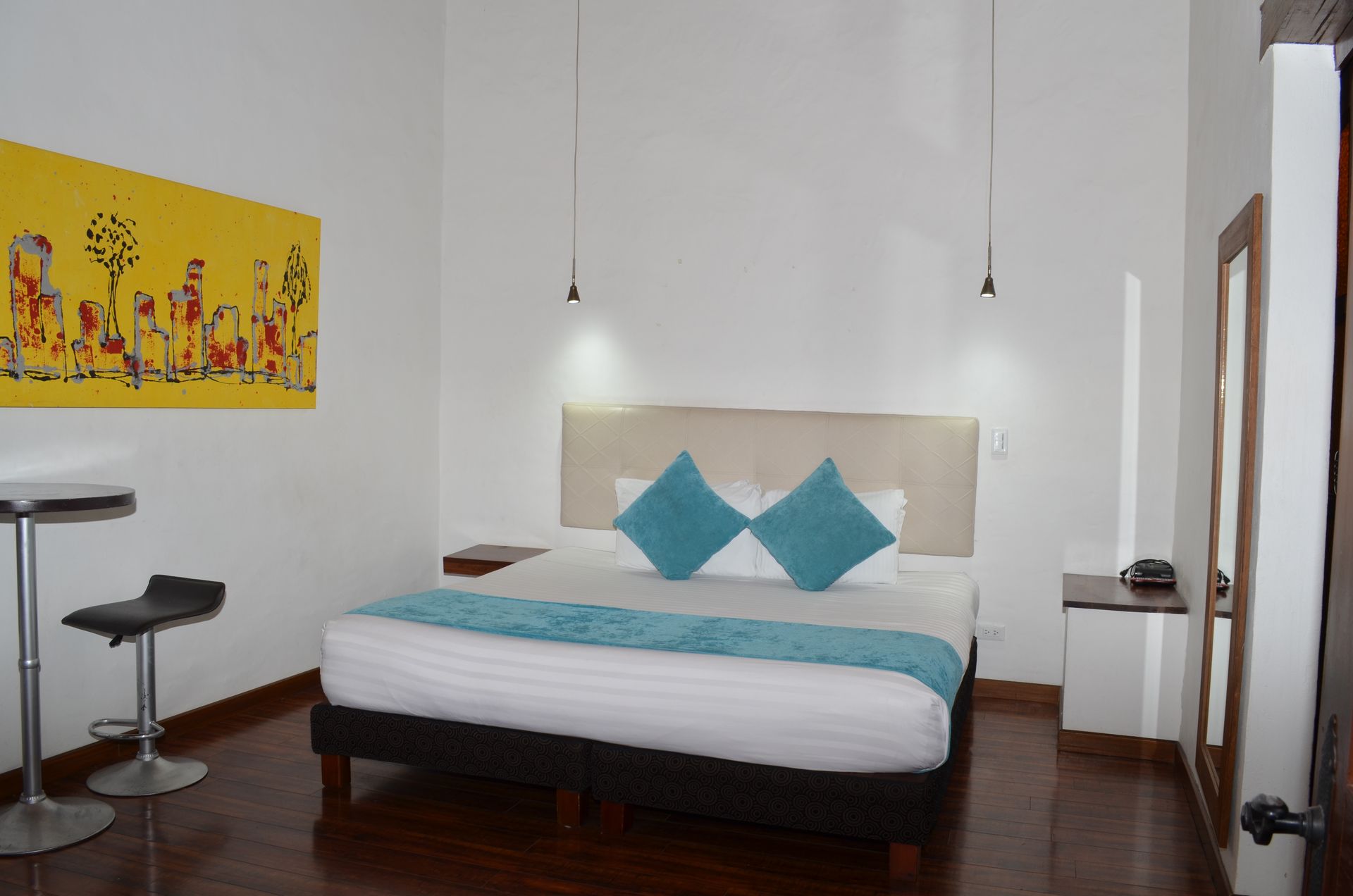Bedroom with a bed, artwork, and minimalist furniture in a well-lit, white-walled room.