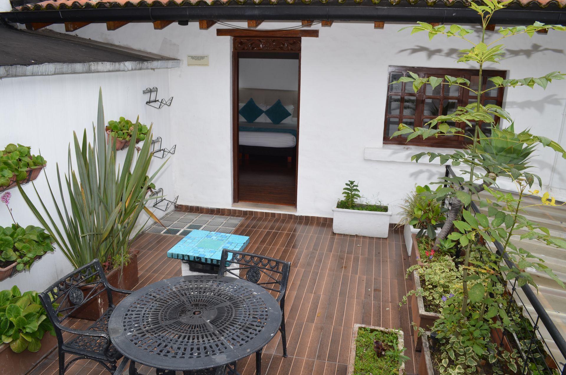 Patio with wooden deck, metal table, potted plants, and open door to bedroom with bed.