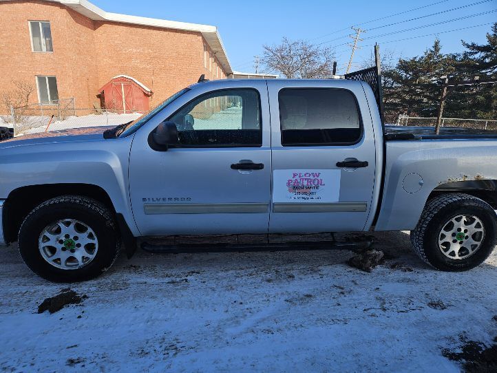 A silver truck is parked in the snow in front of a brick building.