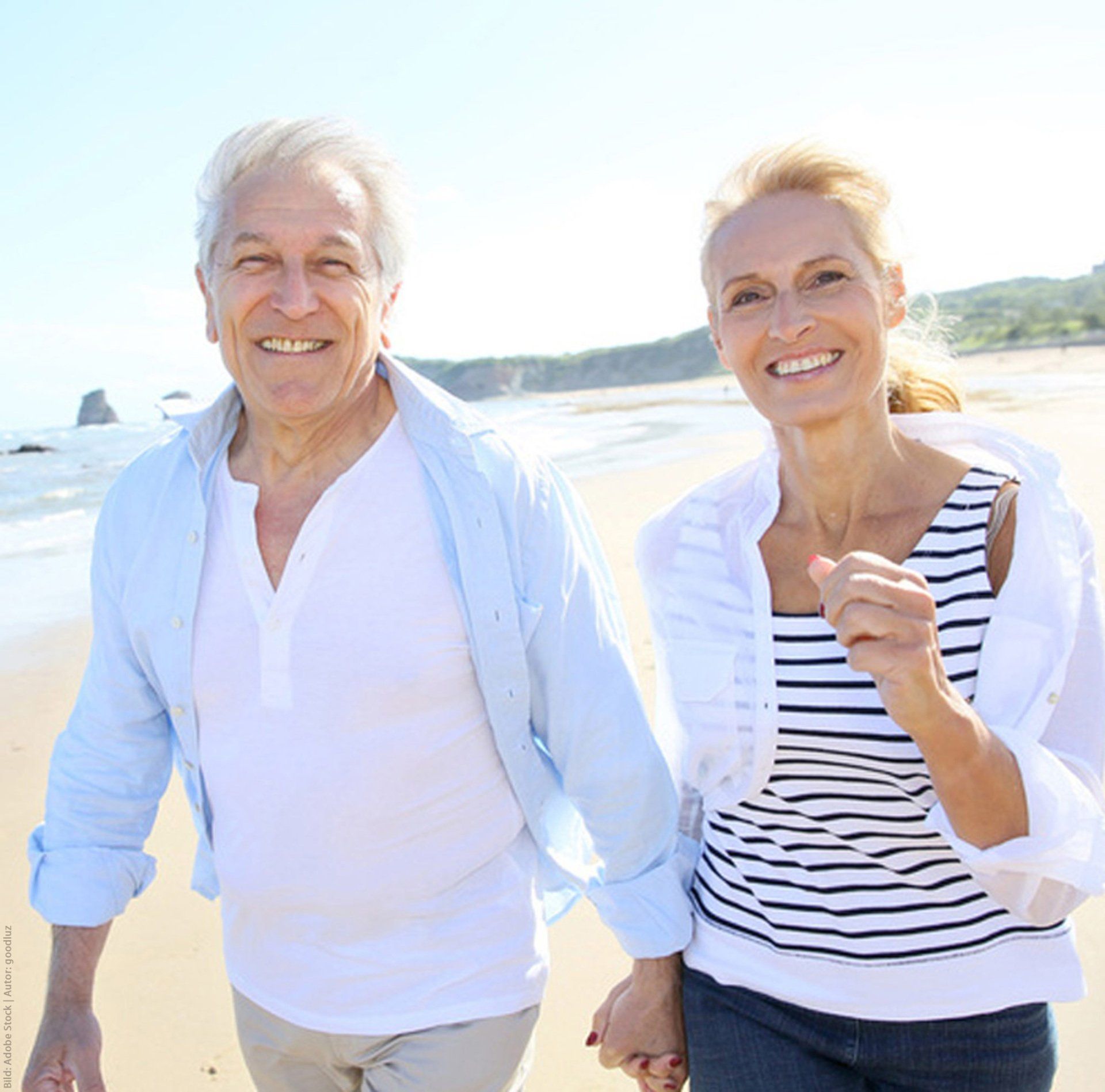 Ein Mann und eine Frau gehen Händchen haltend am Strand spazieren.
