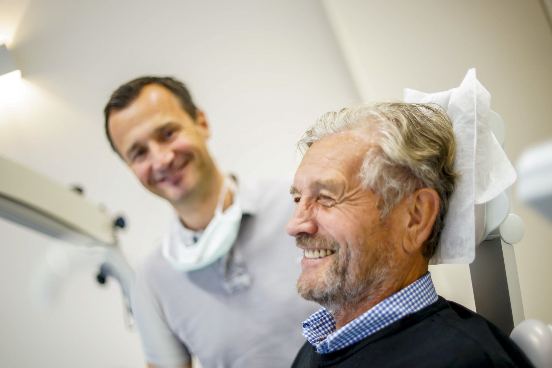 A man is smiling while sitting in a dental chair next to a dentist.