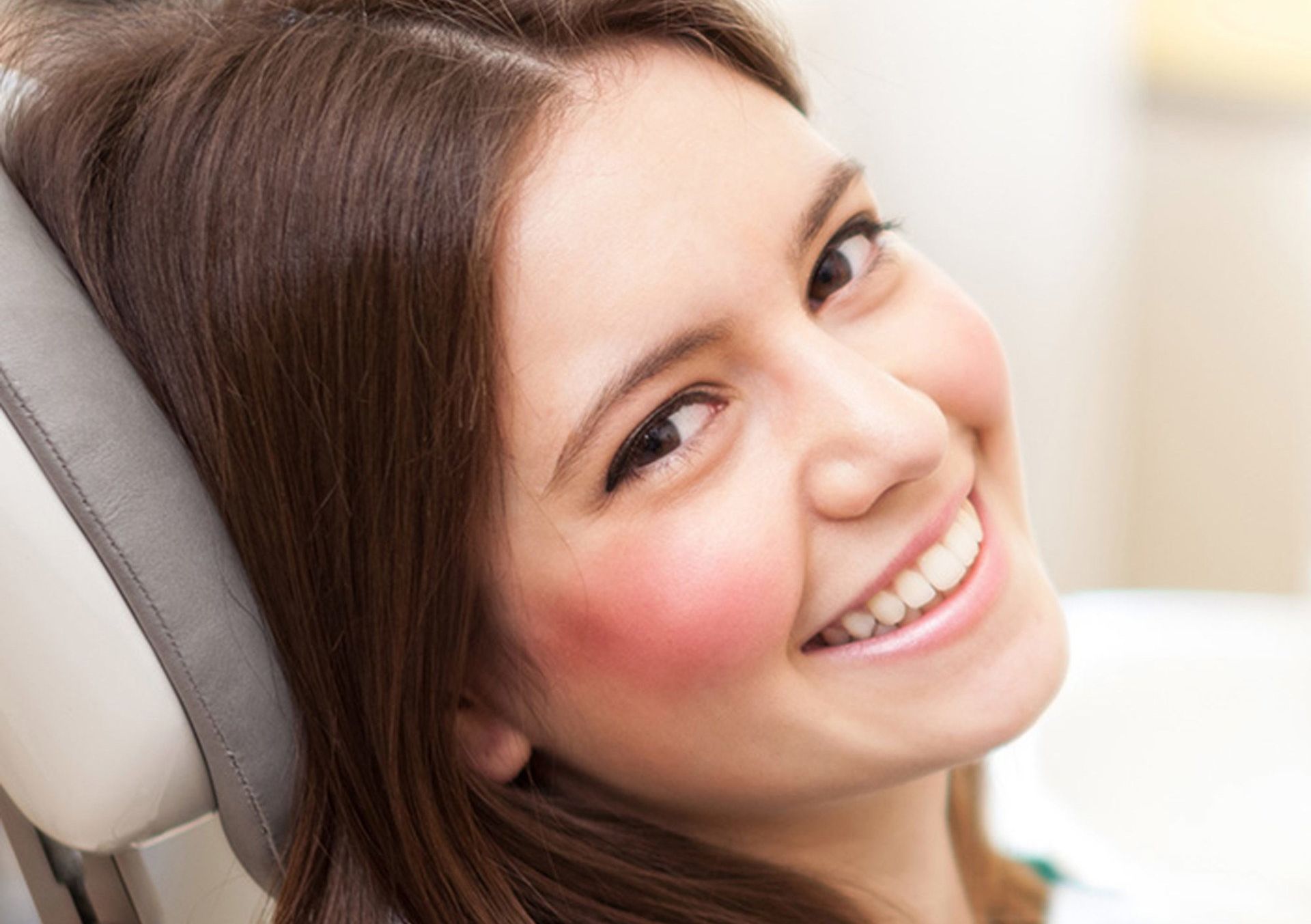 A woman is smiling while sitting in a dental chair.