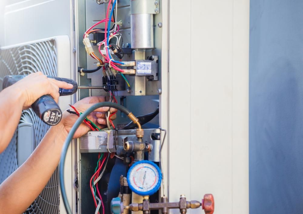 A Man is Working on an Air Conditioner With a Screwdriver — Power & Data Support Services In Tablelands, QLD