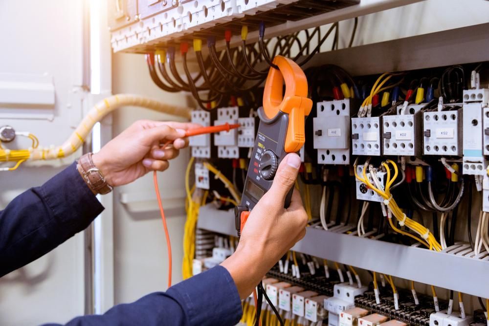 An Electrician is Working on an Electrical Panel With a Clamp Meter — Power & Data Support Services In Manunda, QLD