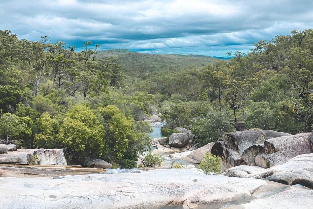A River Runs Through a Lush Green Forest Surrounded by Rocks and Trees — Power & Data Support Services In Mareeba, QLD