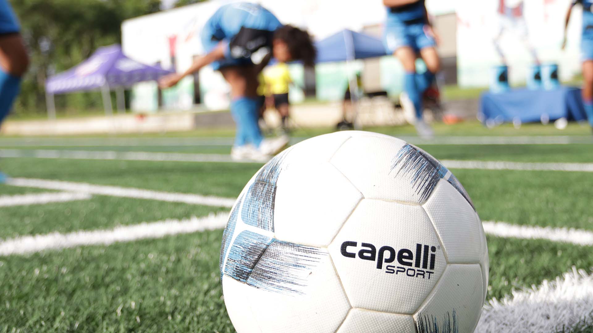 Soccer ball on field with blurred players in the background.