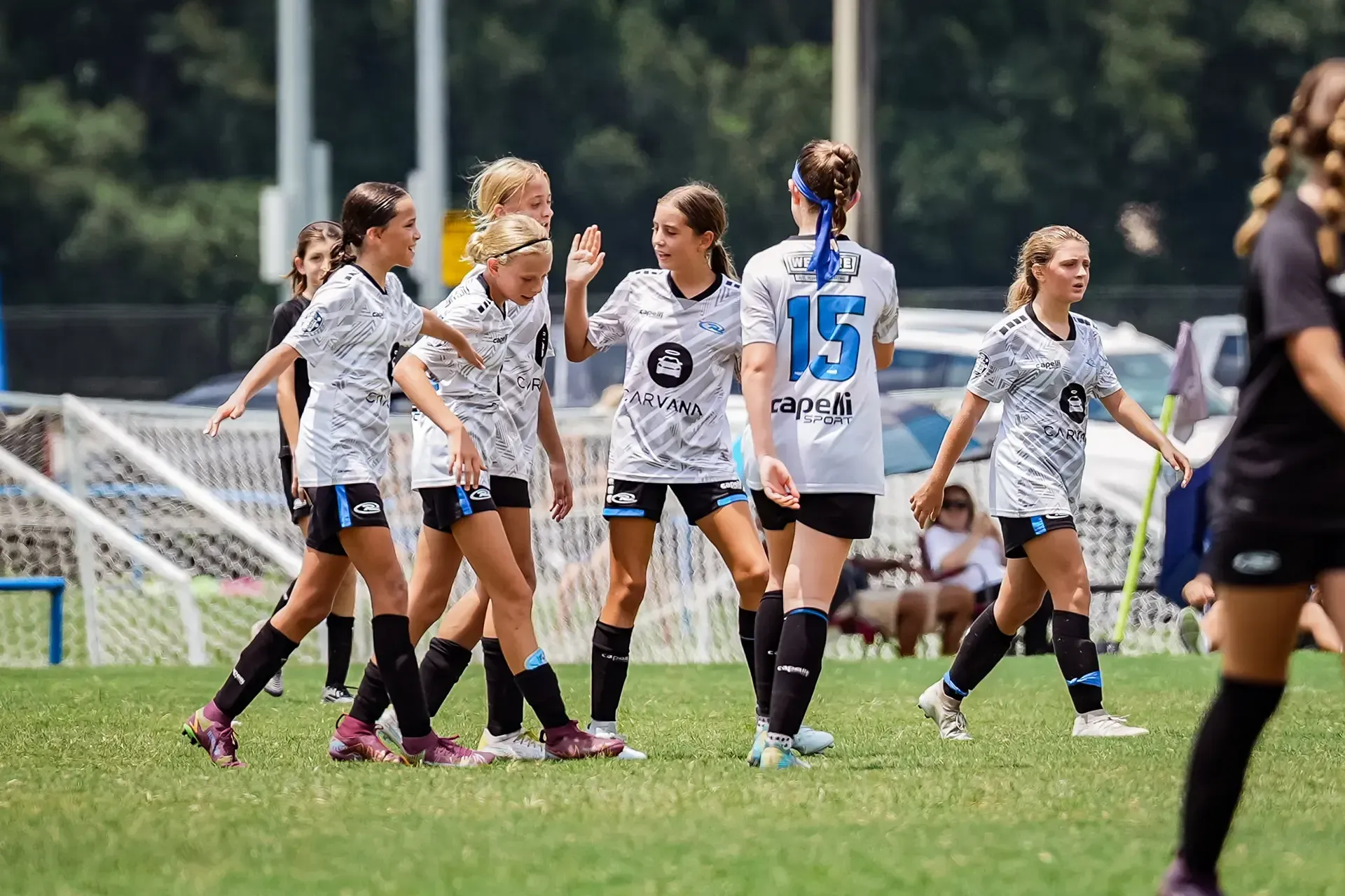 Soccer team celebrating on a green field. Players in matching jerseys, some smiling, with blue and black accents.