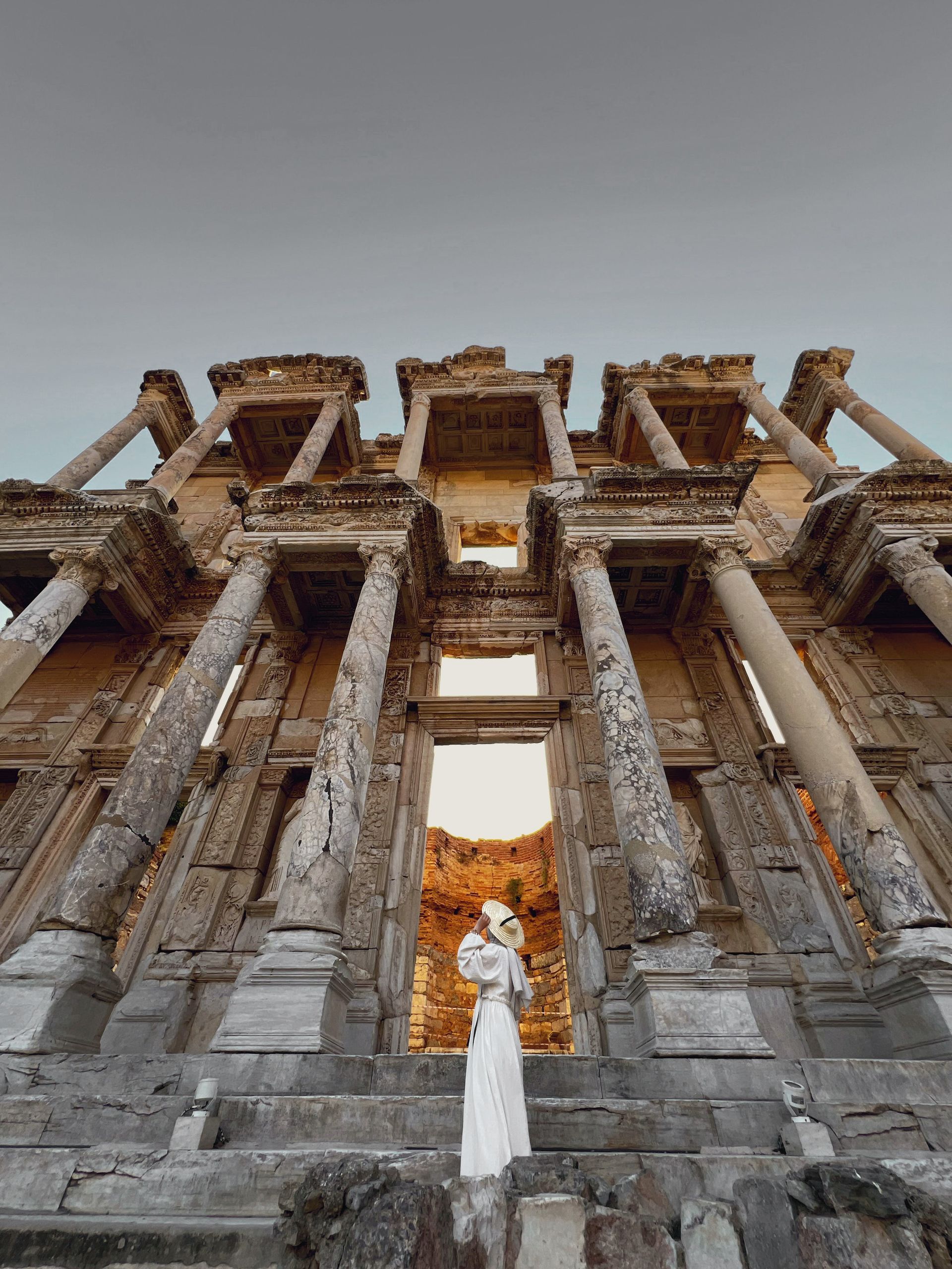 A woman in a white dress is standing on the steps of an ancient building.