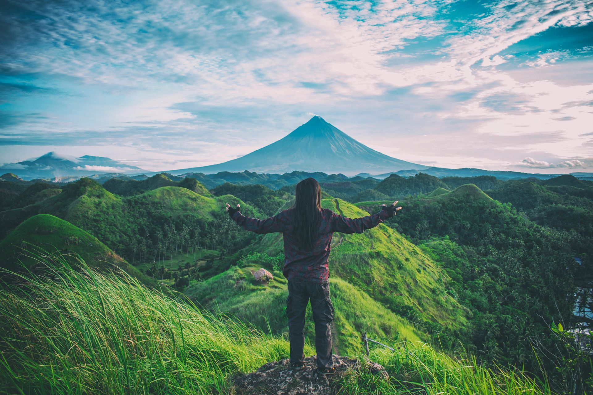 A woman is standing on top of a mountain with her arms outstretched.
