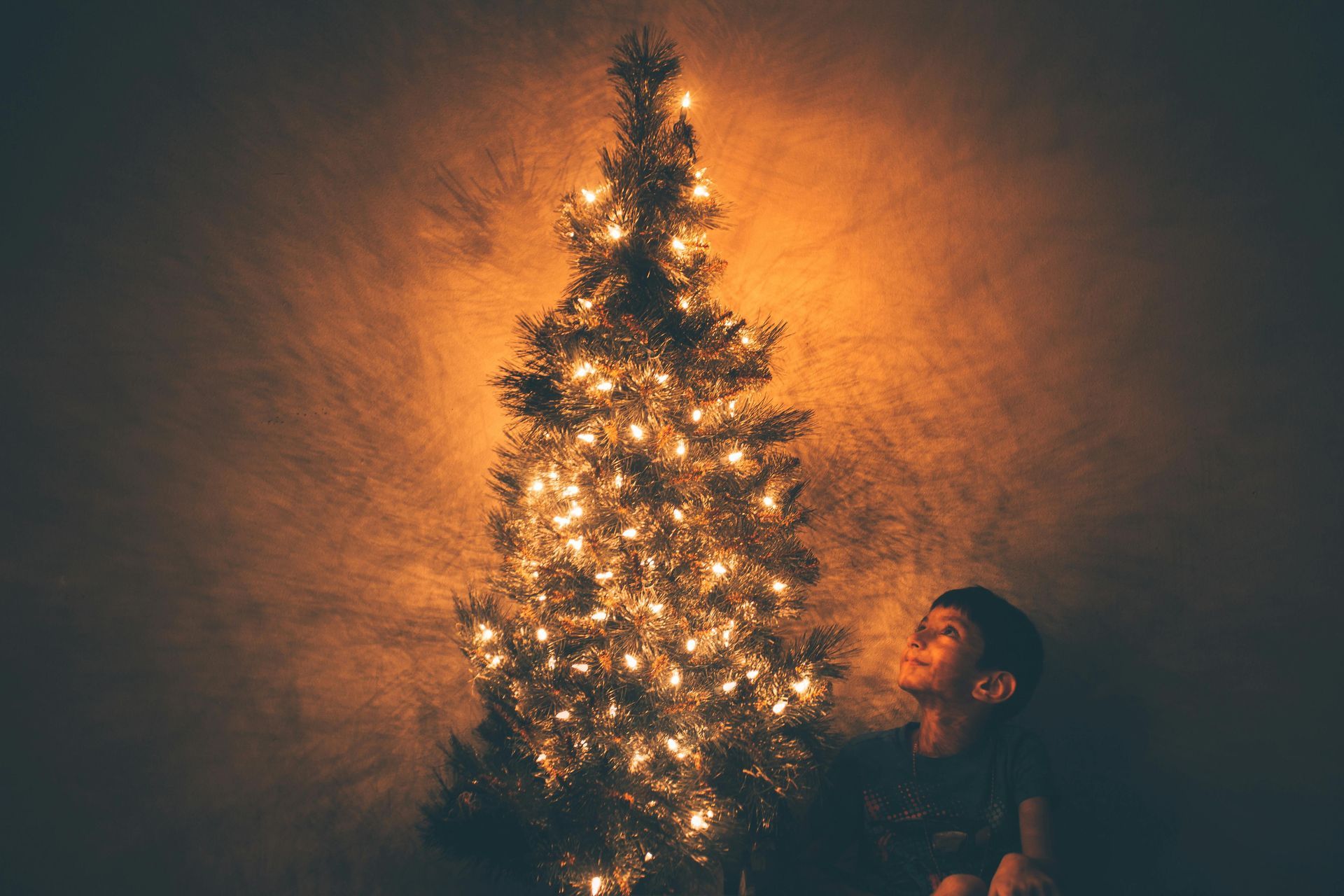 A man is sitting in front of a lit up christmas tree.