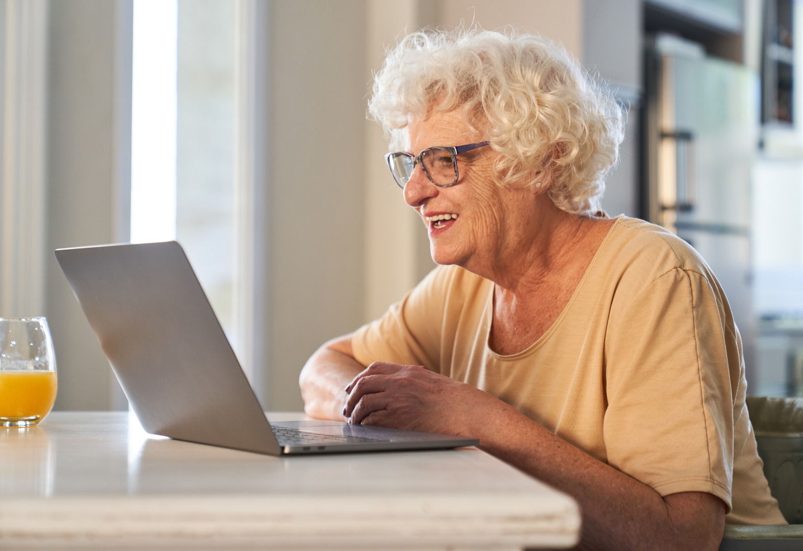 An elderly woman is sitting at a table using a laptop computer.