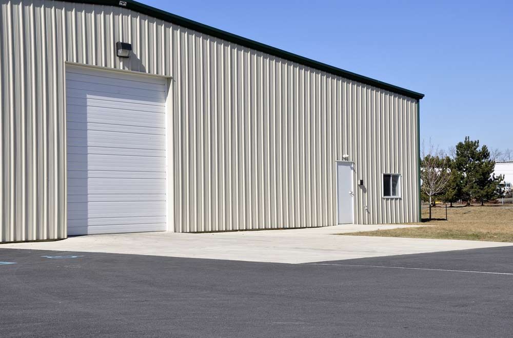 A Large Metal Building With A White Garage Door — Shop Fittings Office Furniture Materials Handling In Gosford, NSW