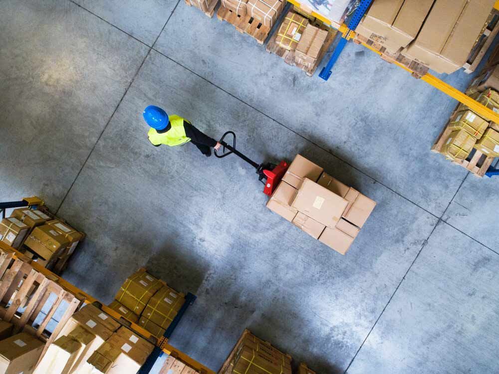 A Man Pushing A Pallet Truck In A Warehouse — Shop Fittings Office Furniture Materials Handling In Blacktown, NSW