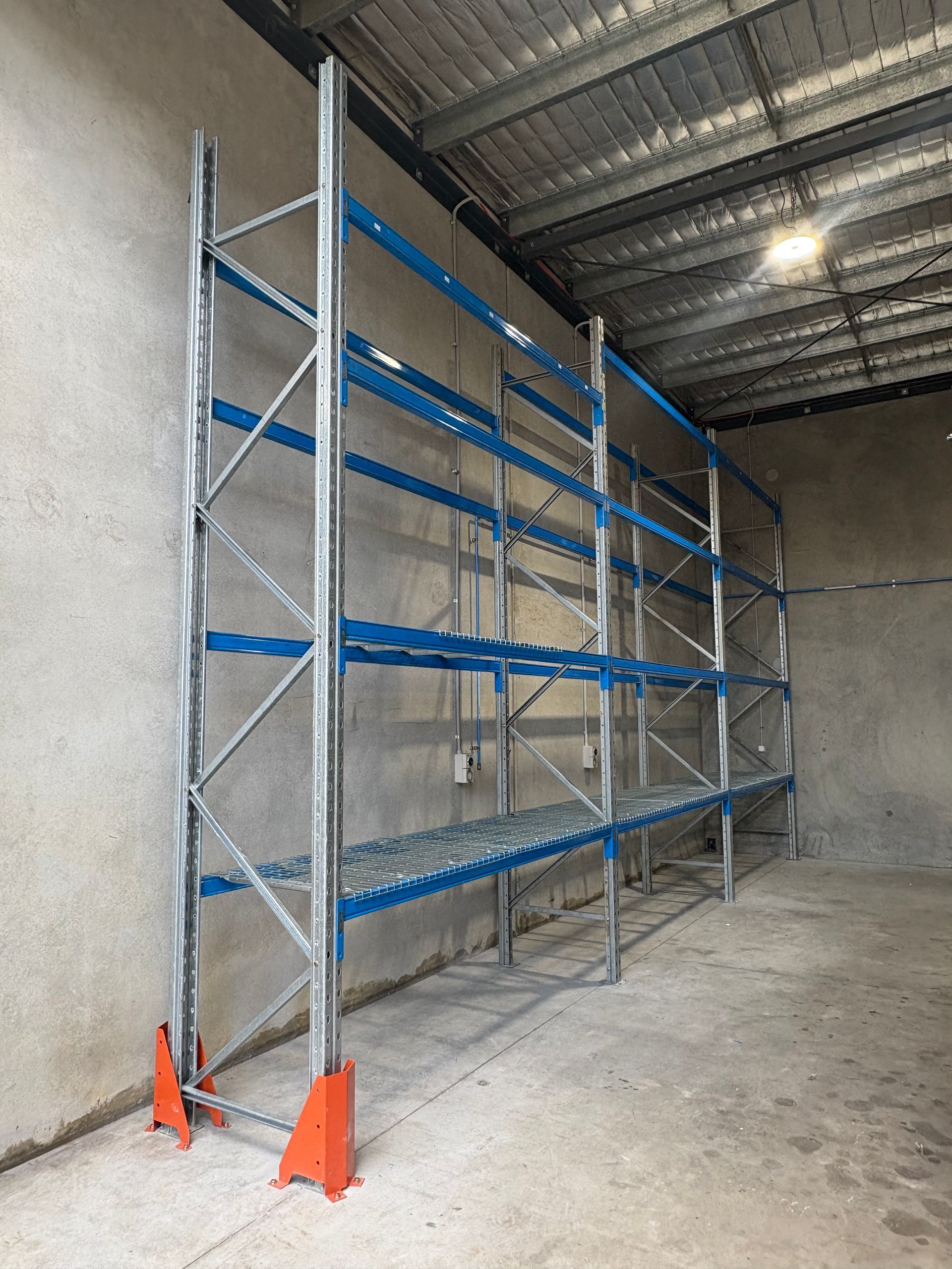 Metal storage rack with blue shelves and orange base supports inside an unfinished concrete warehouse. — Shop Fittings Office Furniture Materials Handling In Gosford, NSW
