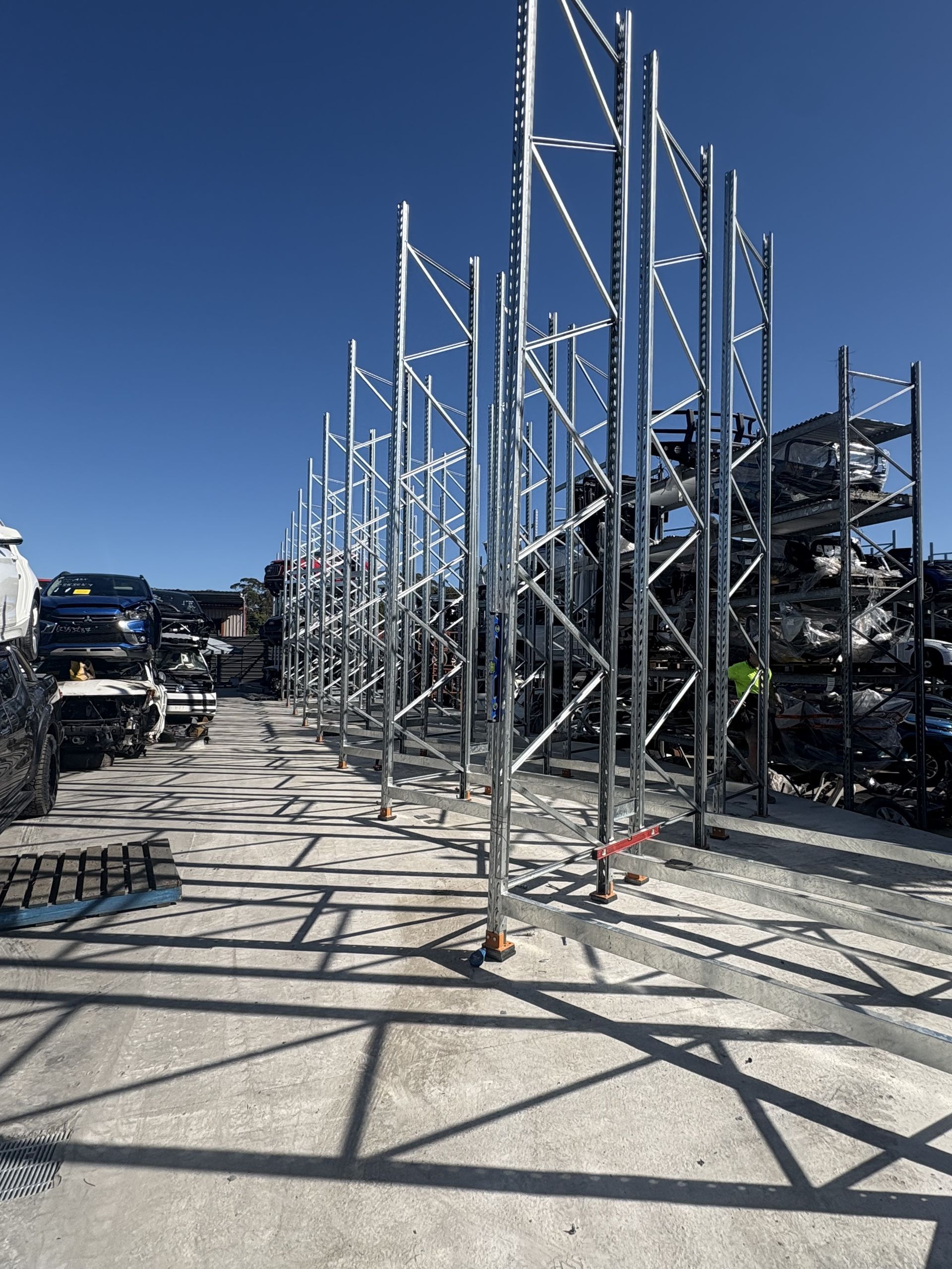 Scaffolding and metal frames line a sunlit outdoor lot with parked cars and blue sky — Shop Fittings Office Furniture Materials Handling In Gosford, NSW