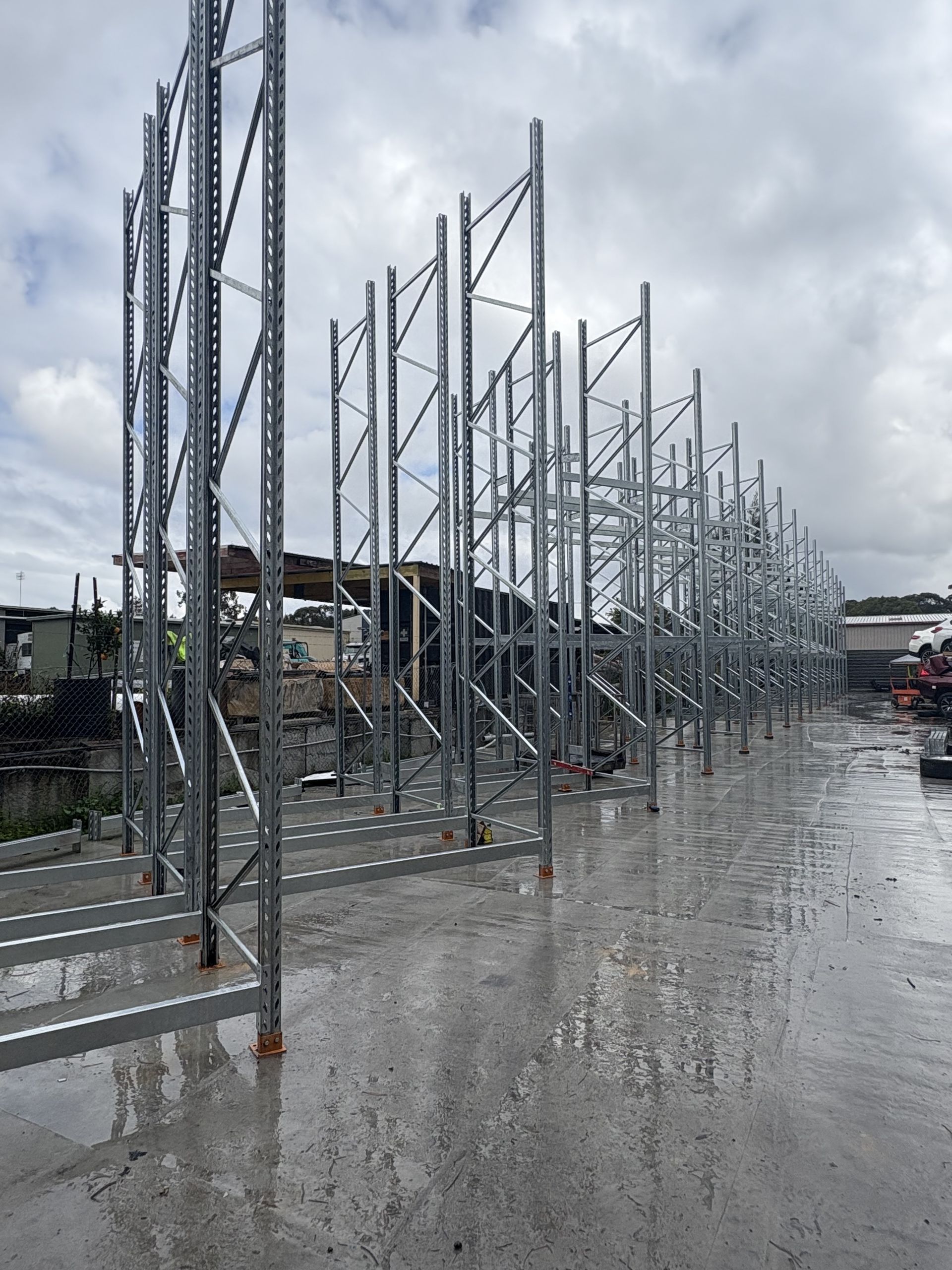 Rows of metal storage racks standing on a wet concrete lot under a cloudy sky