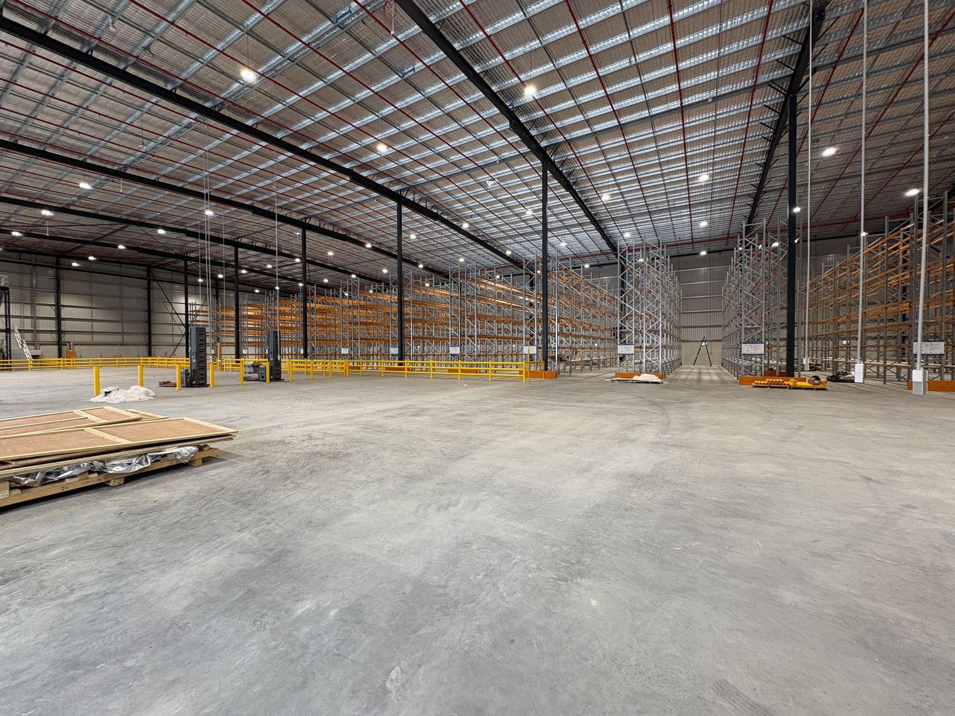 Empty warehouse interior with concrete floor, steel beams, and stacked pallets along the walls — Shop Fittings Office Furniture Materials Handling In Gosford, NSW
