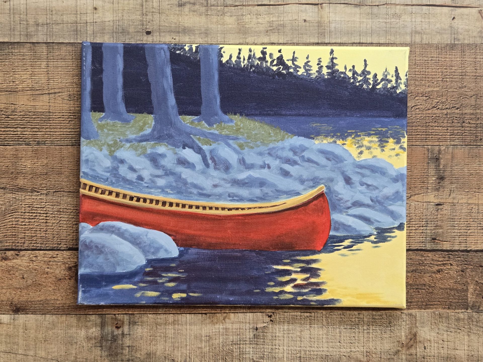 Red canoe on a calm lake beside rocks and pine trees at dusk.