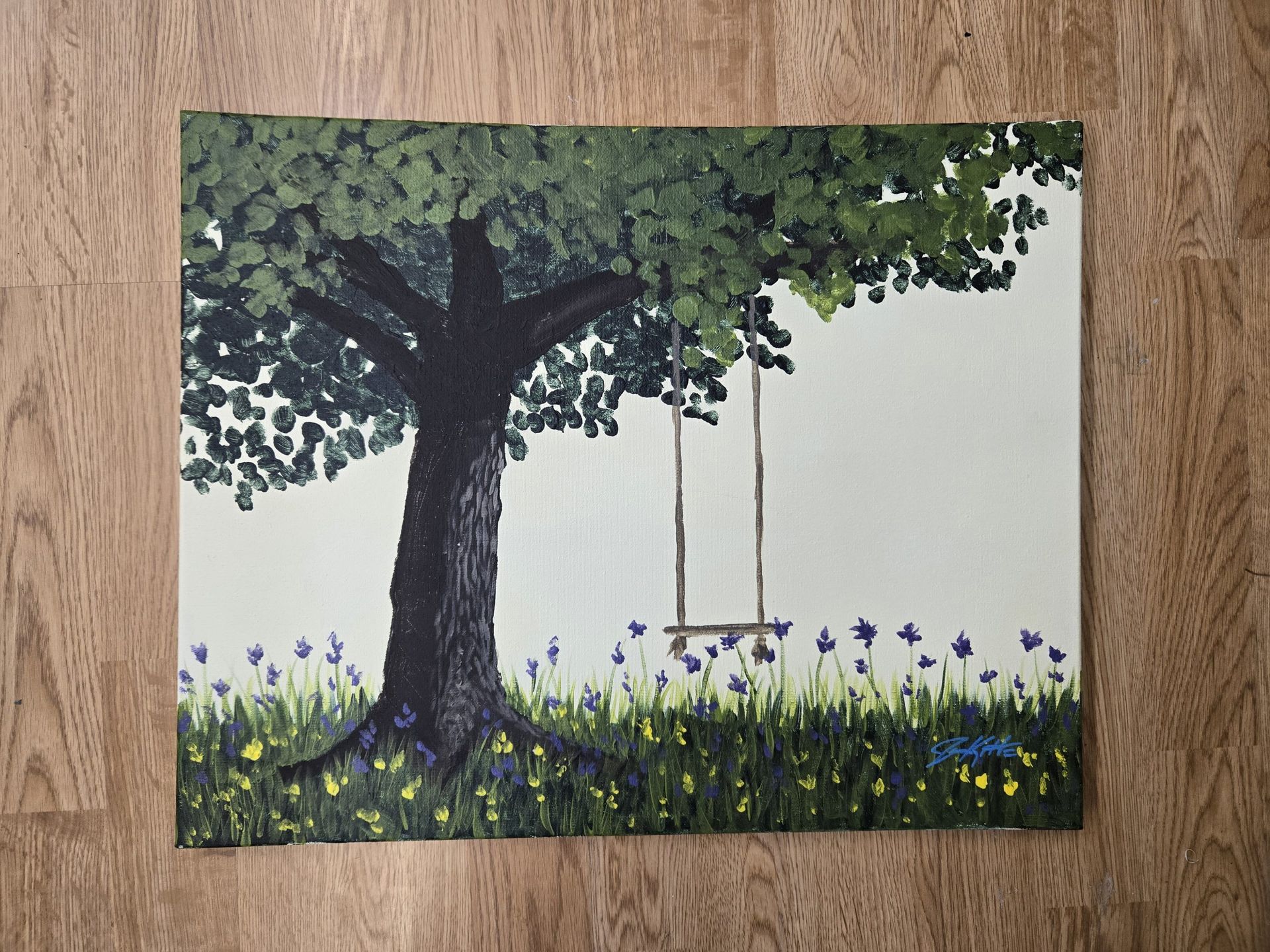 Tree with dense green foliage beside a simple swing over a grassy field of purple flowers.