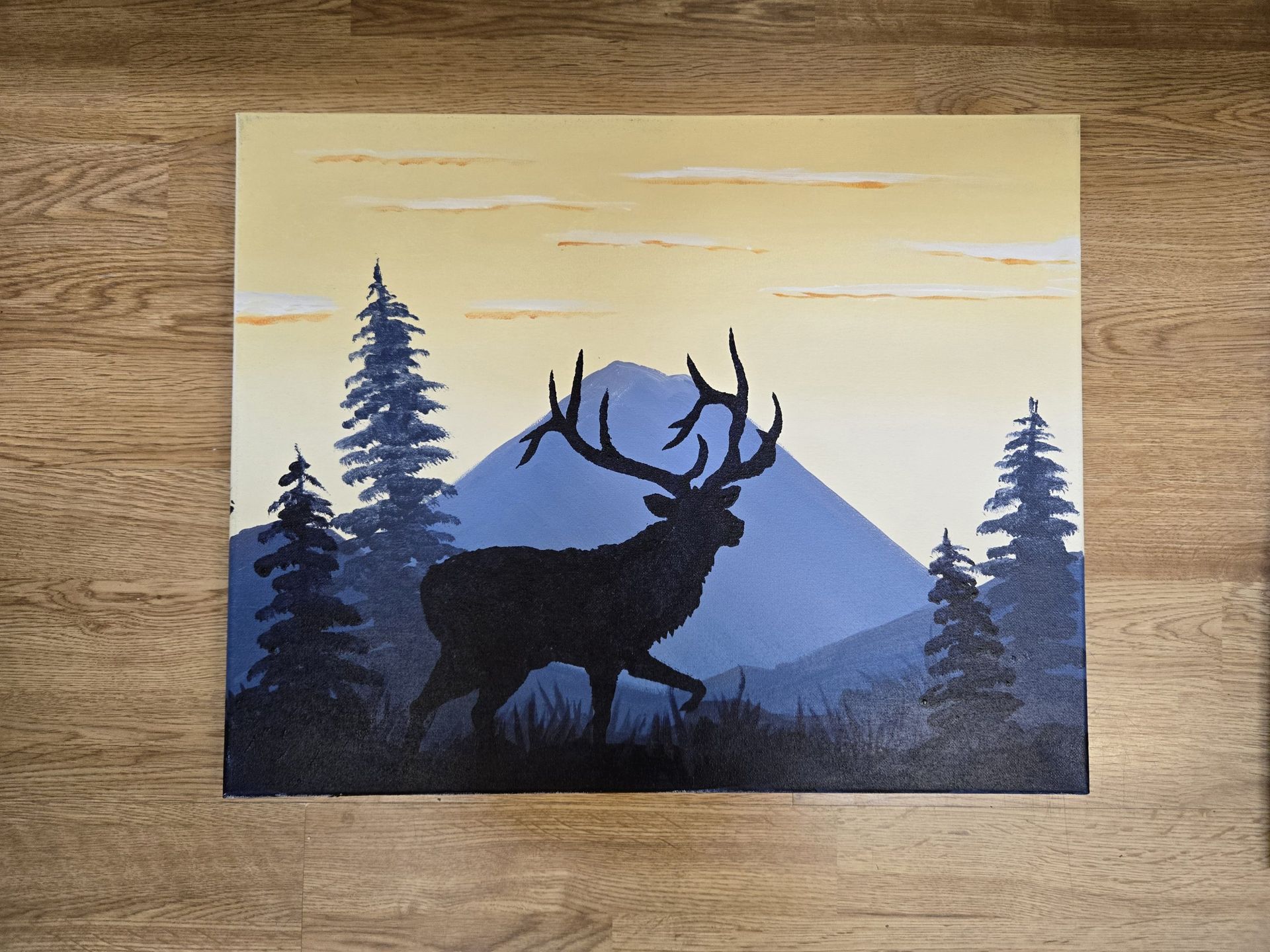 Silhouette of a stag in front of blue mountains and pine trees under a pale sky.