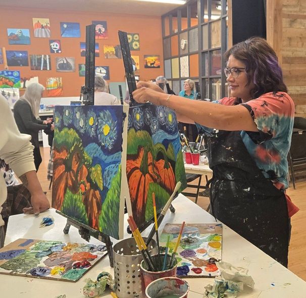 Person painting colorful landscapes on easels in an art studio class