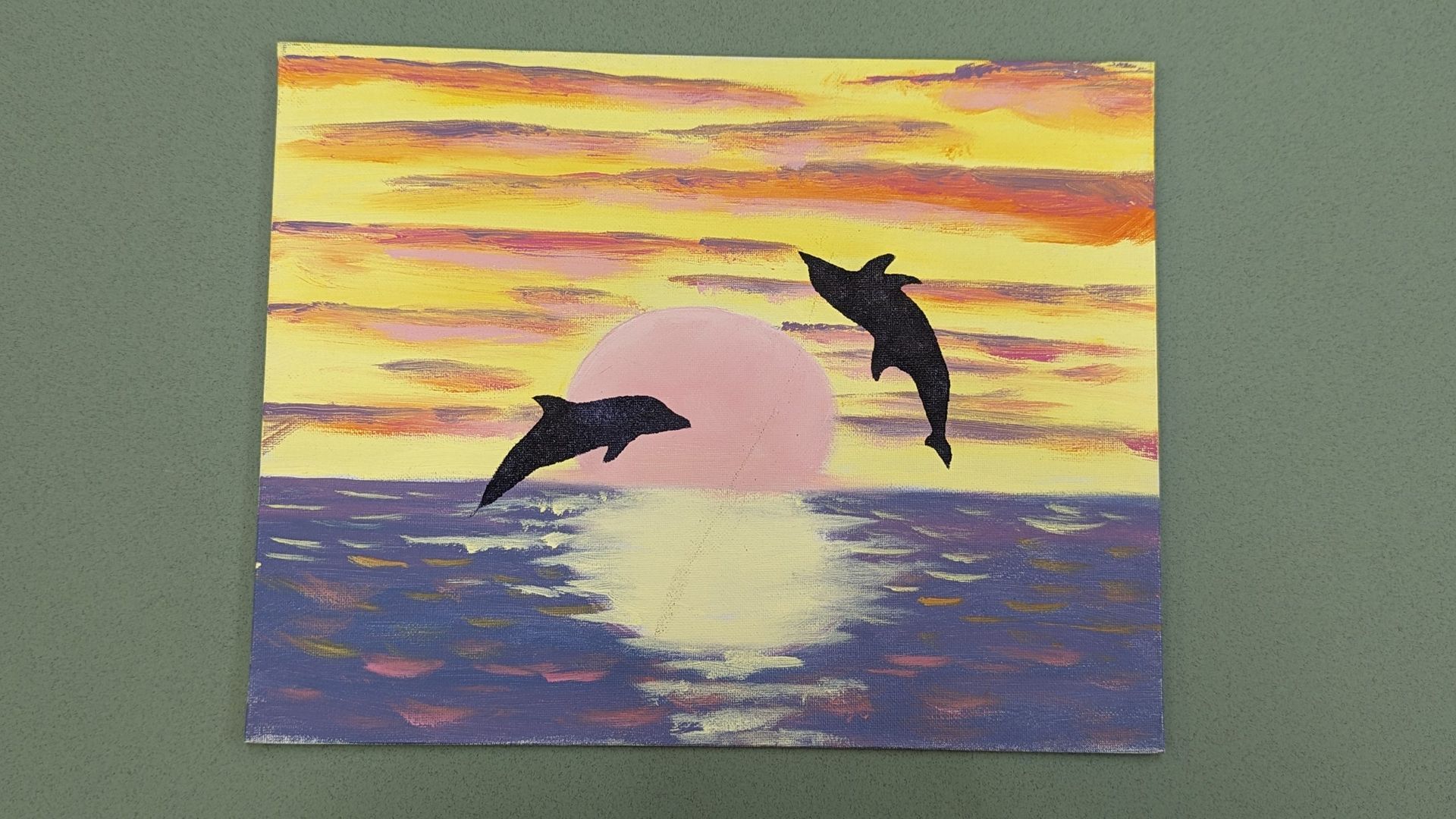 Sunset painting with two dolphins leaping over a purple sea and a pink sun reflection