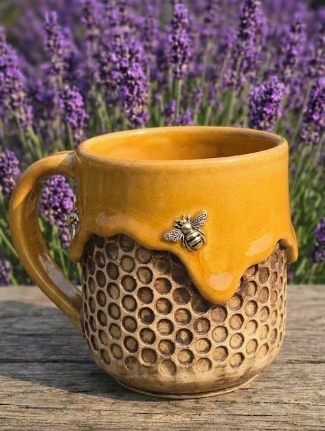 Yellow honeycomb-textured mug with a bee accent, sitting on a wooden surface before purple flowers