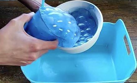 Hands pouring water from a blue cup into a white bowl inside a blue tray