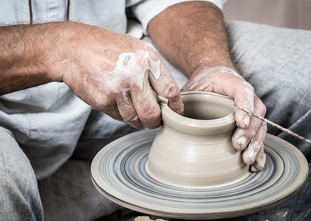 Hands shaping a clay pot on a pottery wheel, with white clay dust on the fingers.