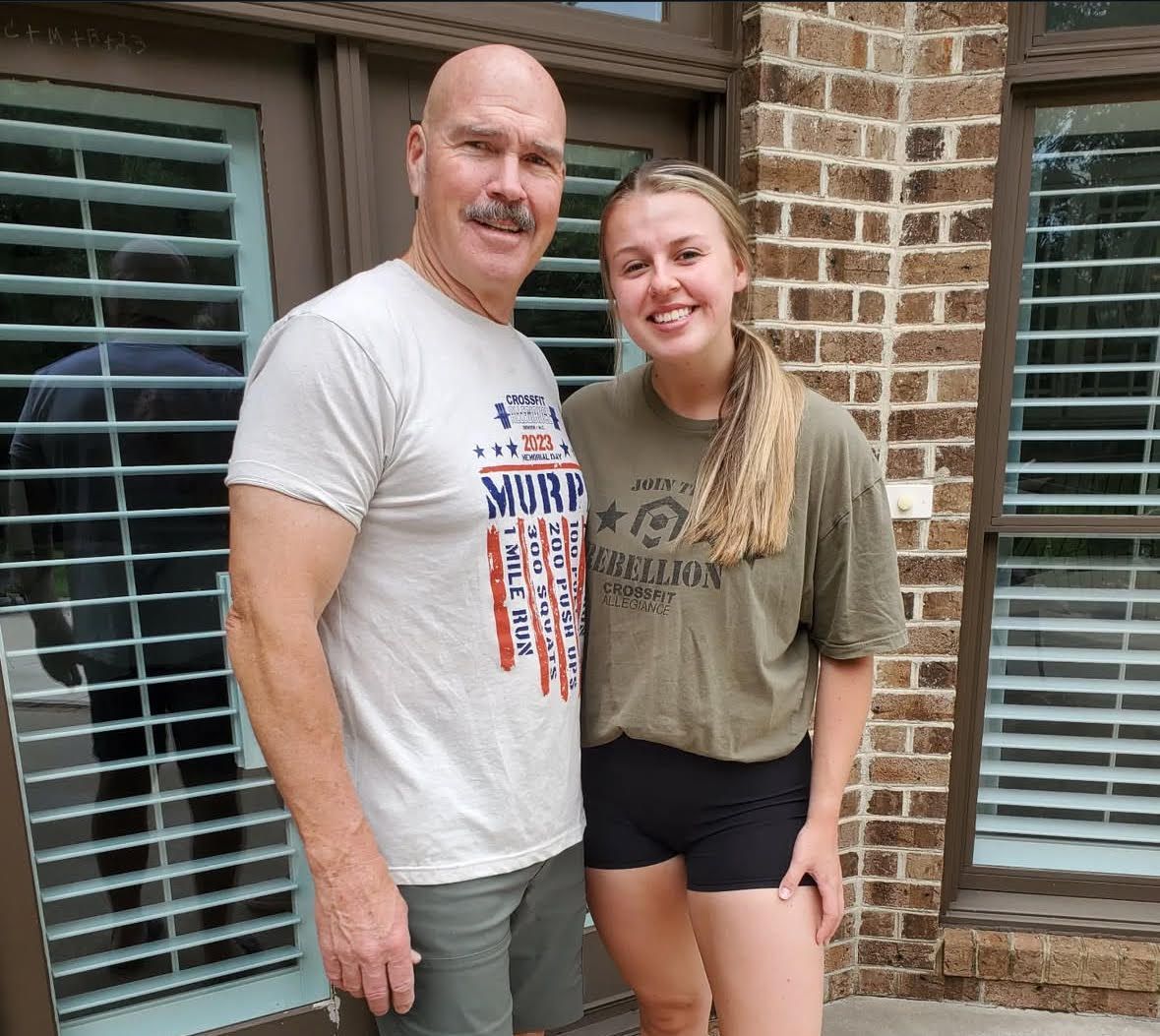 Man and woman standing together outside by brick wall, both smiling.