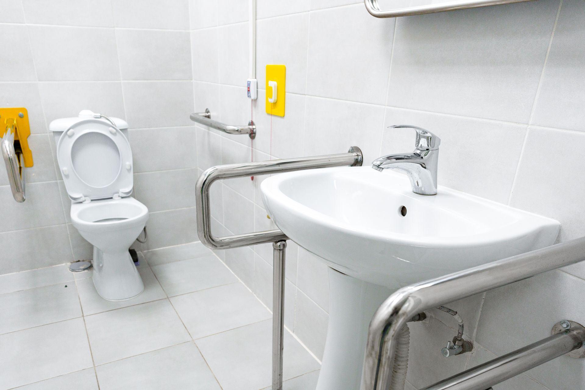 A bathroom with a toilet , sink and handrails.
