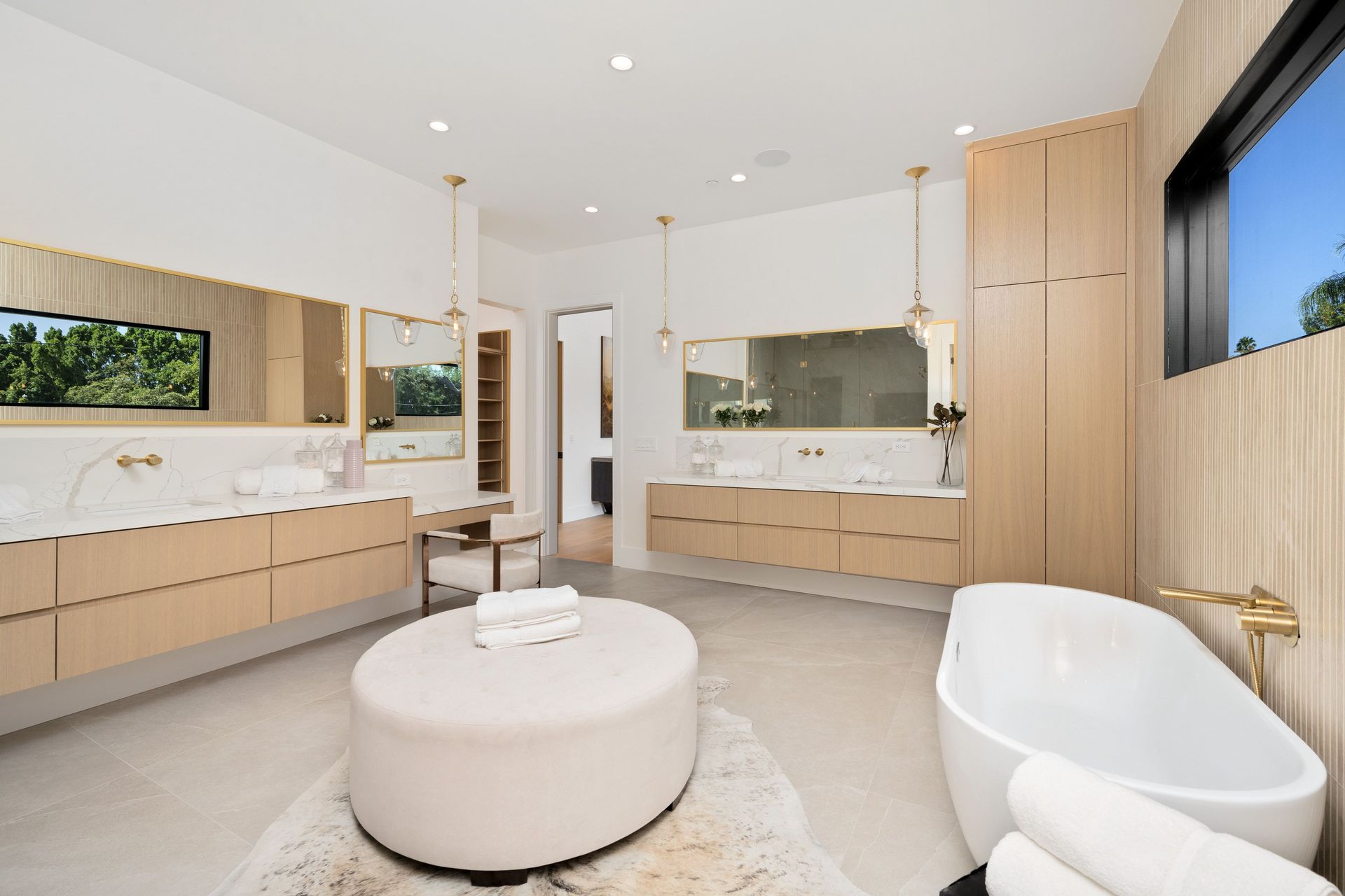 A bathroom with a tub , sinks , mirrors and a ottoman.