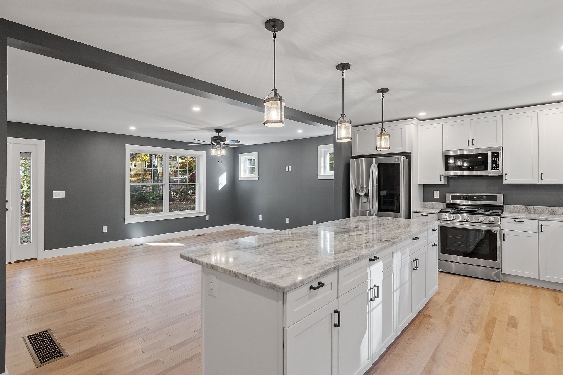 A kitchen with white cabinets , granite counter tops , stainless steel appliances and hardwood floors.