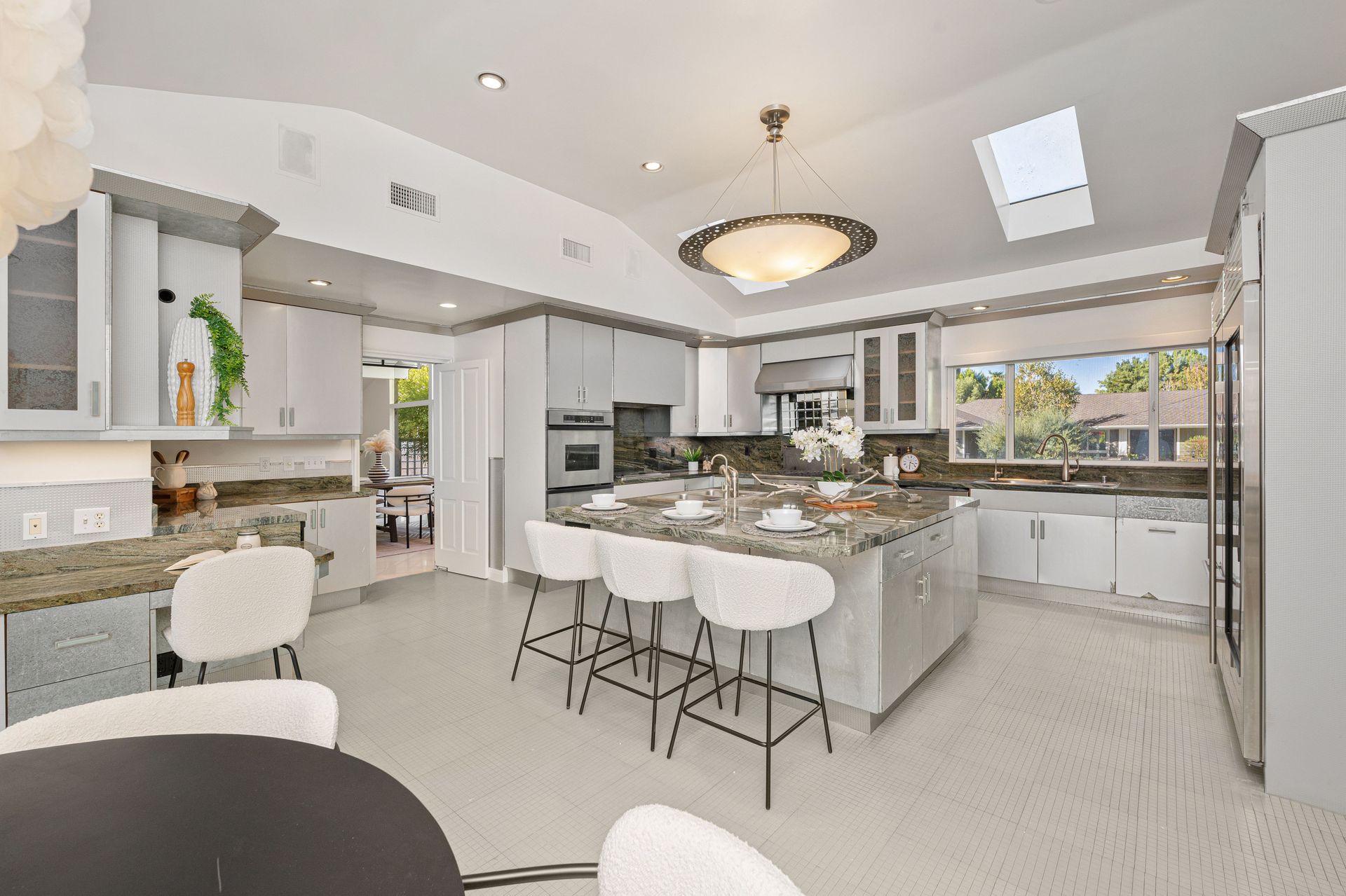 A kitchen with white cabinets , granite counter tops , stools and a large island.