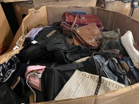 A cardboard box filled with lots of handbags and shoes.