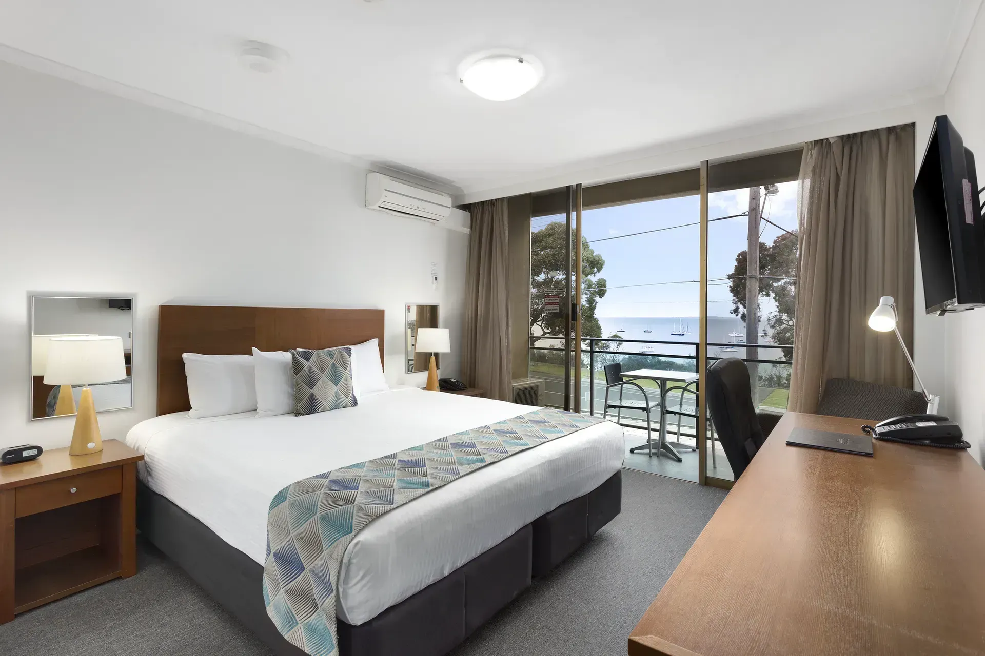 Modern hotel room with a bed, desk, and sliding doors overlooking a balcony and ocean view