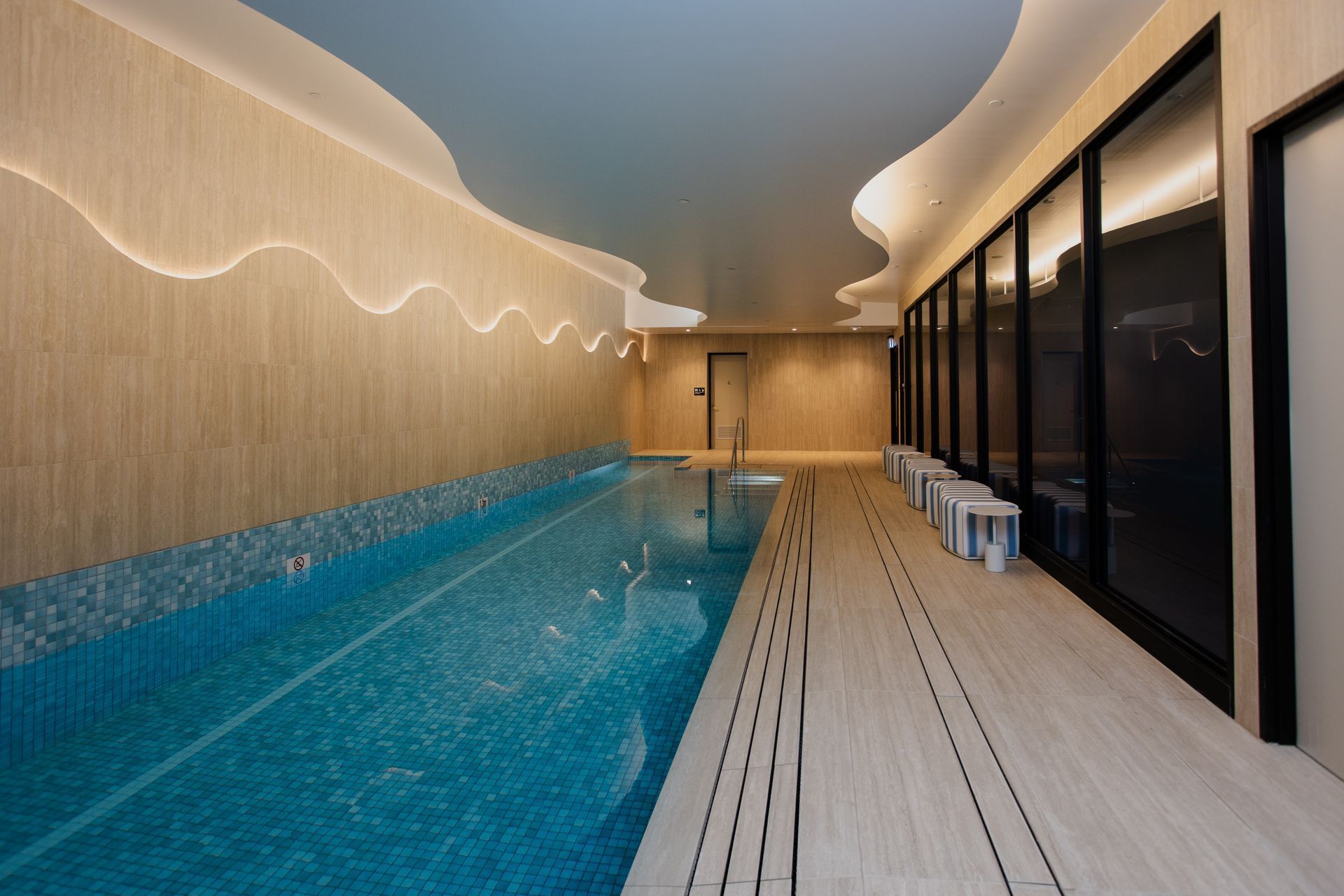 Indoor pool with turquoise water, wood deck, and glass-walled lounge area