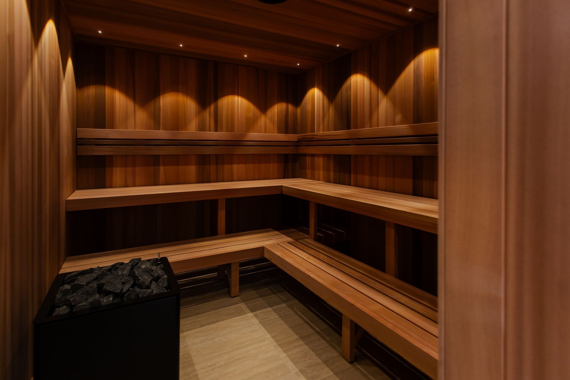 Wood-paneled sauna with L-shaped wooden benches and warm ambient lighting