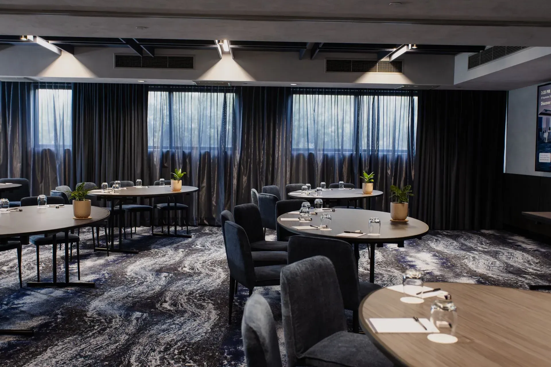 Elegant banquet room with round tables, gray chairs, and floor-to-ceiling curtains under soft lighting